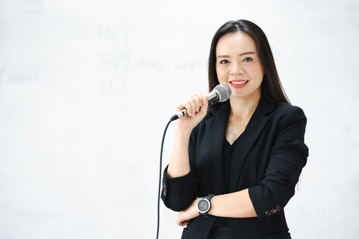 A middle-aged Asian woman teacher hold the microphone in classroom white board at University