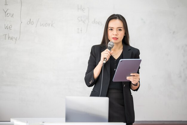 대학 교실 화이트보드에 태블릿을 들고 있는 중년 아시아 여성 교사