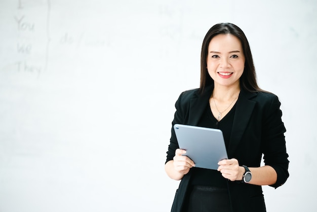 대학 교실 화이트보드에 태블릿을 들고 있는 중년 아시아 여성 교사