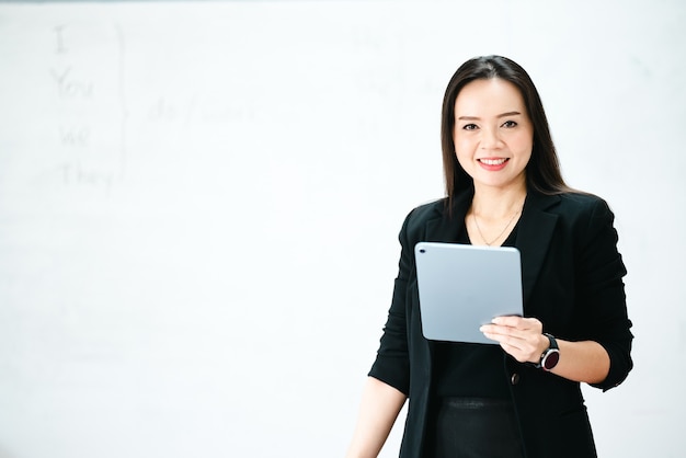 A middle-aged Asian woman teacher holding a tablet in classroom white board at University