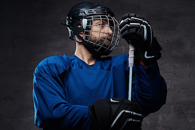 Middle-aged bearded hockey player wearing full sports equipment with a hockey stick