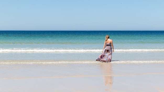 Middle-aged blonde woman in a dress relaxes on the beach