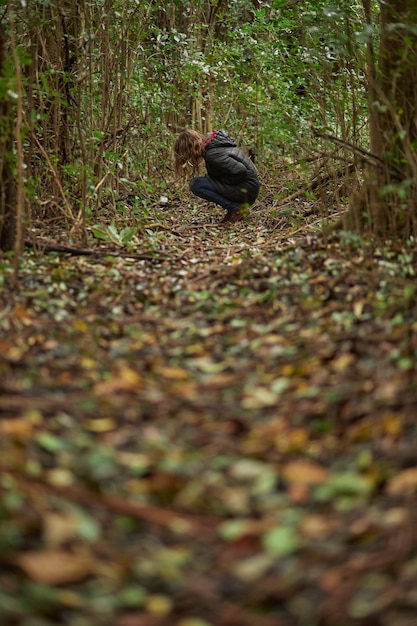 Donna bionda di mezza età nella foresta per godersi la natura in inverno. accovacciato guardando le piante. tra gli alberi.