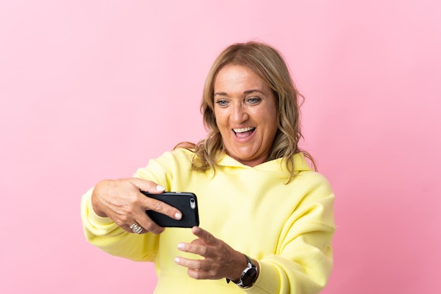 Middle aged blonde woman on isolated pink playing with the mobile phone