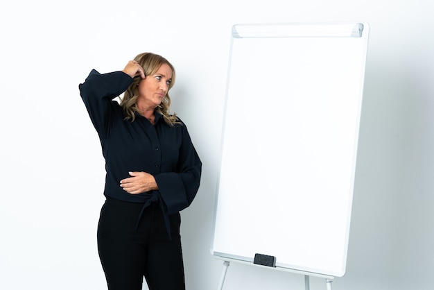 Middle aged blonde woman over isolated white background giving a presentation on white board and having doubts with confuse face expression