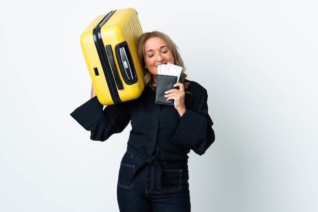 Middle aged blonde woman over isolated white background in vacation with suitcase and passport