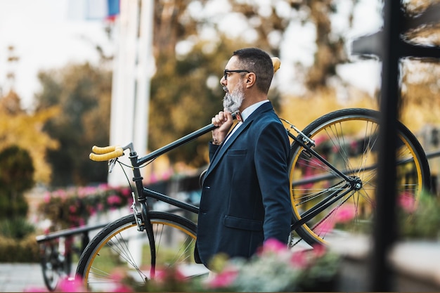 中年のビジネスマンが自転車で通勤し、階段を越えて自転車を肩に乗せている。