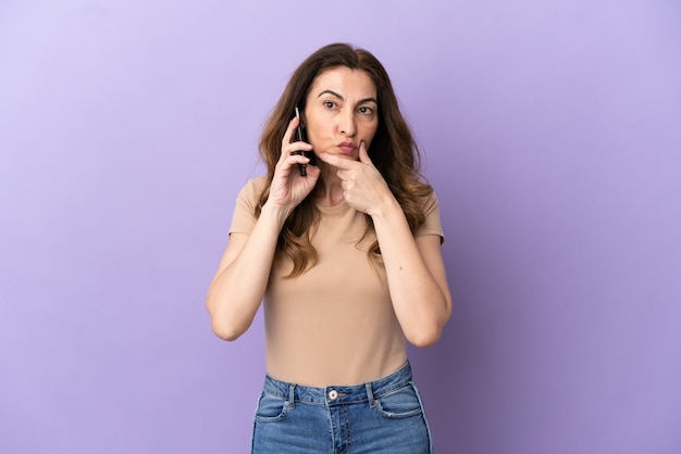 Middle aged caucasian woman using mobile phone isolated on purple background thinking