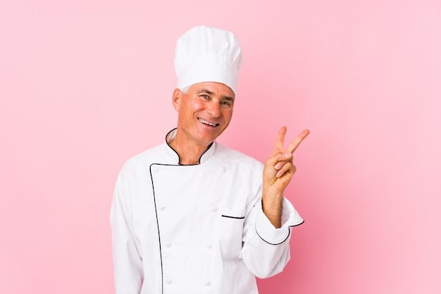 Middle aged cook man isolated joyful and carefree showing a peace symbol with fingers.