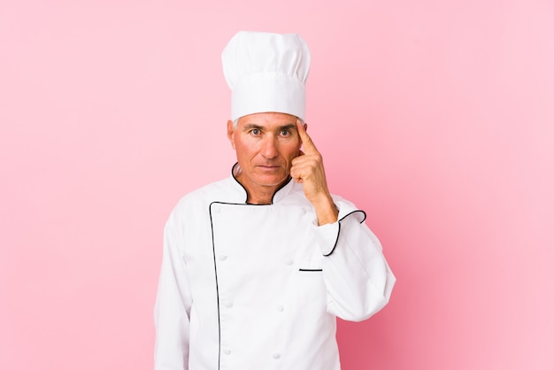 Middle aged cook man isolated pointing temple with finger, thinking, focused on a task.