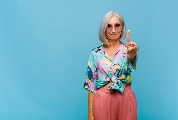 Middle aged cool woman smiling and looking friendly, showing number one or first with hand forward, counting down