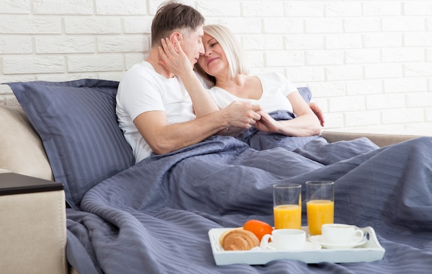 Middle aged couple drink coffee in bed.