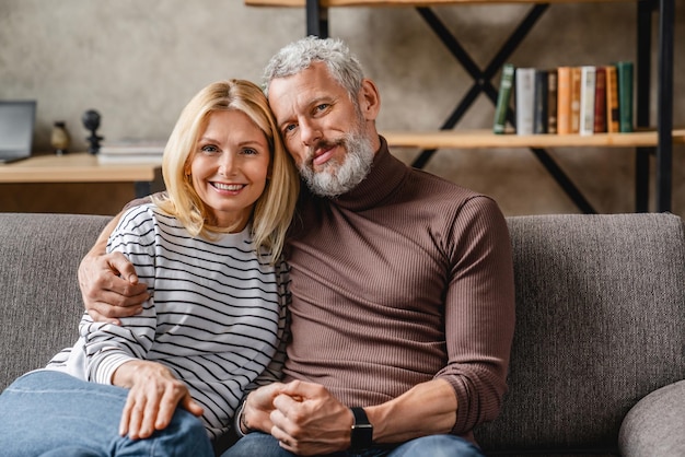 Middle aged couple relaxing on couch smiling at camera at home in living room