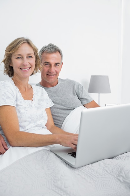 Middle aged couple using their laptop together in bed