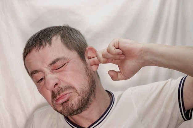 A middle-aged European man with a beard picks his ear with his finger.