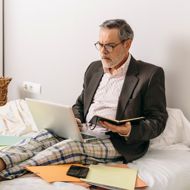 Middle-aged executive attending a business meeting via videoconference from the office mounted on his home bed