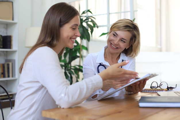 Photo middle aged female doctor therapist in consultation with patient in office.