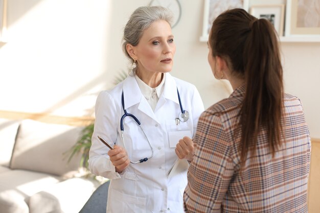 Photo middle aged female doctor therapist in consultation with patient in office.