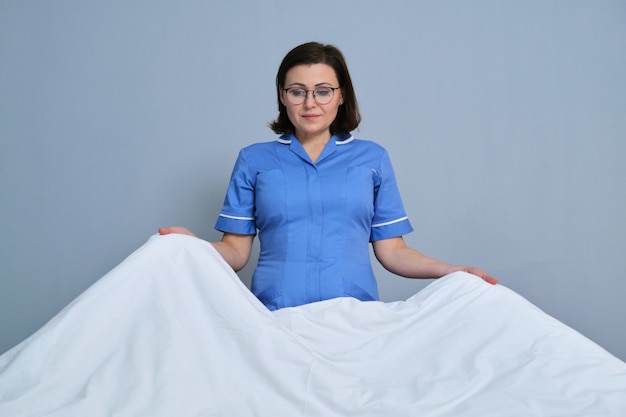 Middle aged female professional maid making bed in hotel room