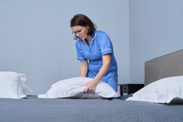 Middle aged female professional maid making bed in hotel room