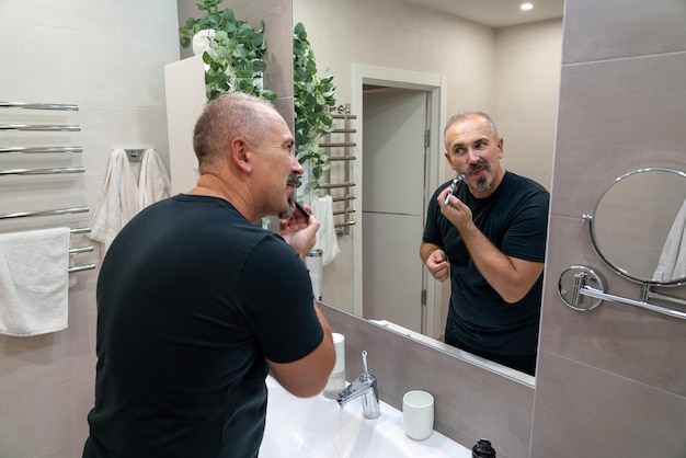 Middle aged handsome man shaving his beard in bathroom