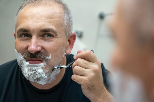 バスルームでひげを剃っている中年のハンサムな男