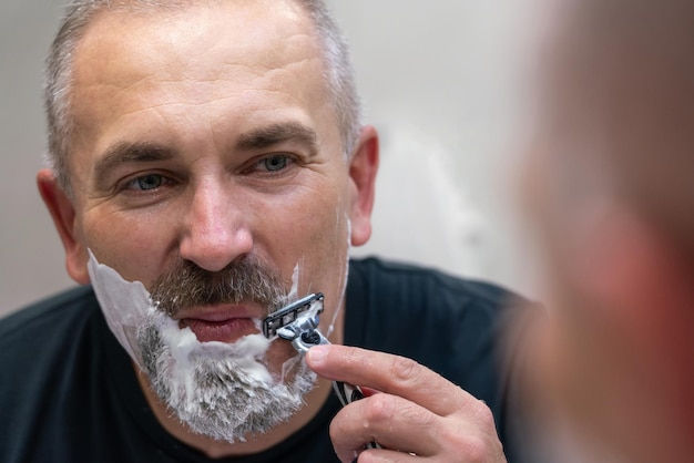 Middle aged handsome man shaving his beard in bathroom