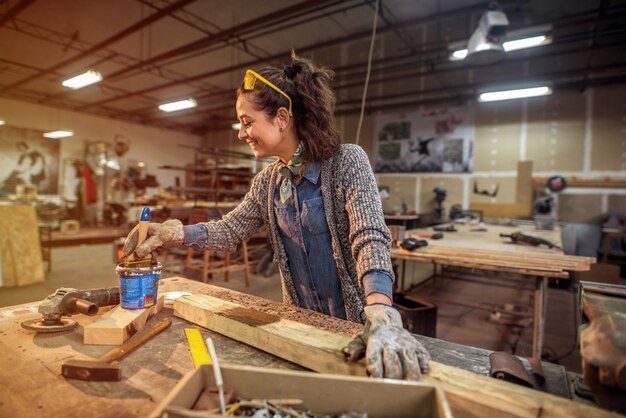 Middle aged happy carpenter painting some wood in her workshop