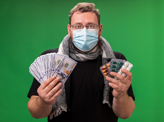 Middle-aged ill male wearing medical mask and scarf isolated on green wall