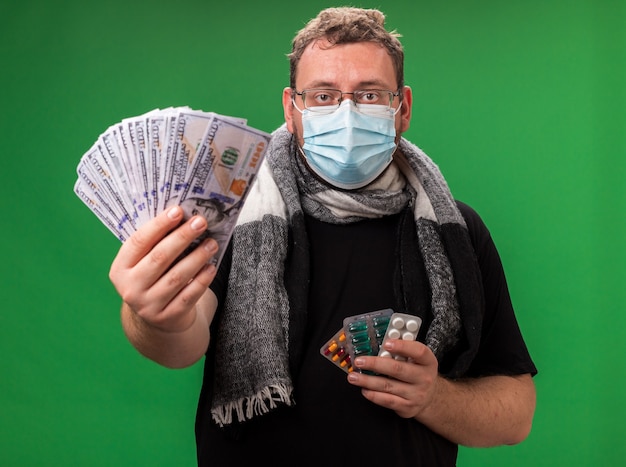 Maschio malato di mezza età che indossa maschera medica e sciarpa isolata sul muro verde