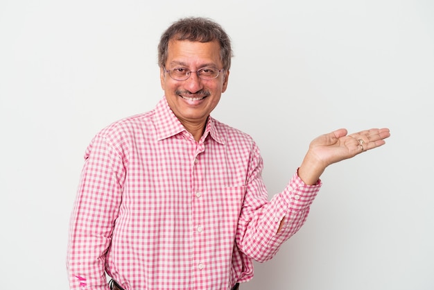 Middle aged indian man isolated on white background showing a copy space on a palm and holding another hand on waist.