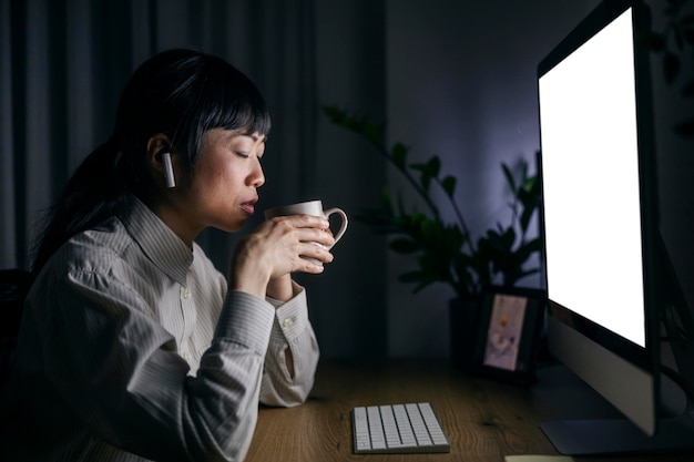 중년 일본인 사업가 여성이 가정 사무실에서 늦게까지 일하고 커피를 마시고 있습니다.