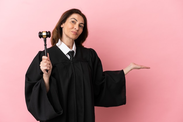 Middle aged judge woman isolated on pink background extending hands to the side for inviting to come