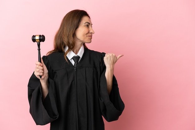 Middle aged judge woman isolated on pink background pointing to the side to present a product