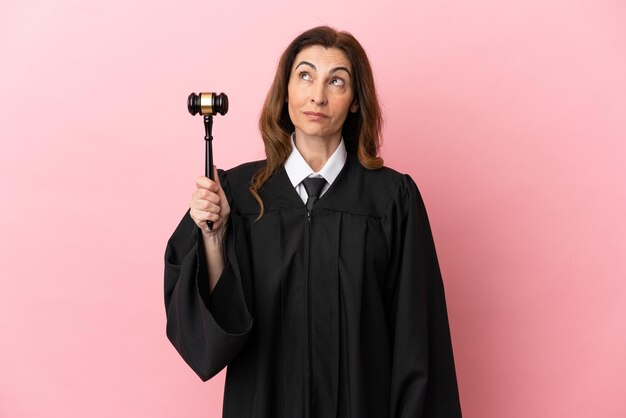 Middle aged judge woman isolated on pink background thinking an idea while looking up