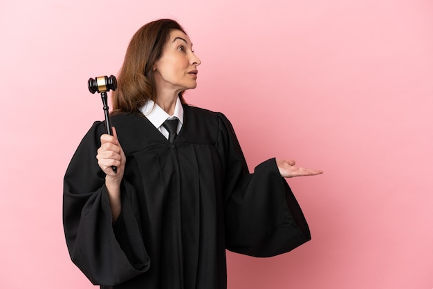 Middle aged judge woman isolated on pink background with surprise expression while looking side