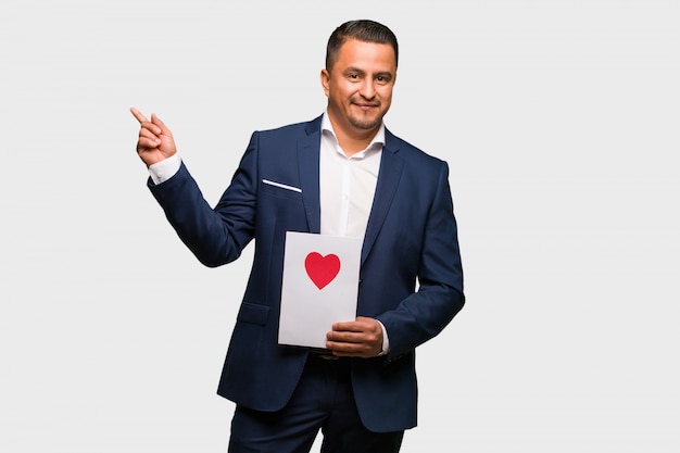 Middle aged latin man celebrating valentines day pointing to the side with finger