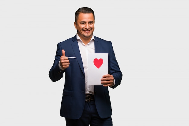 Middle aged latin man celebrating valentines day smiling and raising thumb up