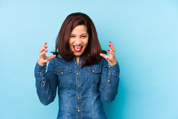 Middle aged latin woman isolated on a blue wall screaming with rage