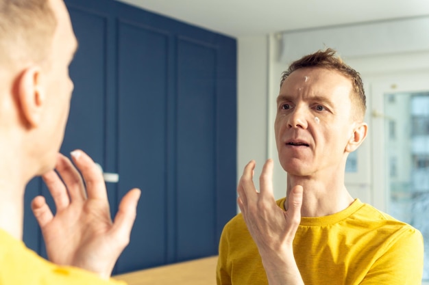 Middle aged man apply moisturizing cream with finger on clear facial areas Male portrait in mirror Skincare concept