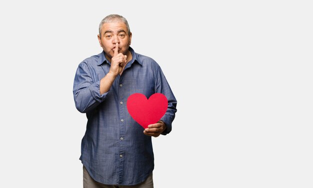 Middle aged man celebrating valentines day keeping a secret or asking for silence