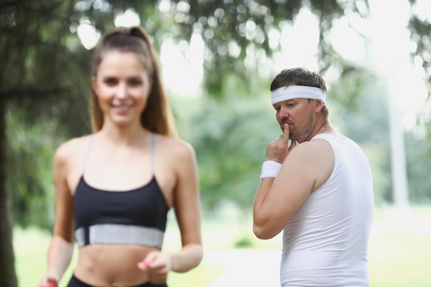 Middle aged man check on young beautiful fit woman running in park