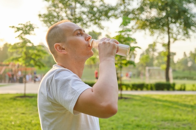 Middle-aged man drinking milk, dairy product from bottle outdoor