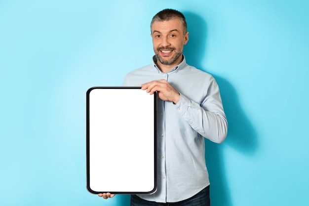 Middle aged man holding big digital tablet on blue background