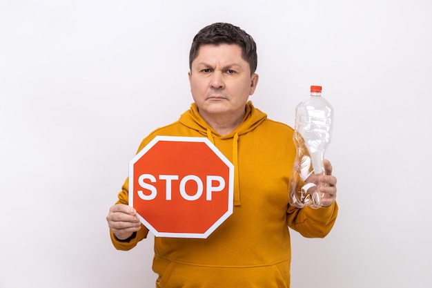 Middle aged man holding plastic bottle and stop red sign worrying about environment