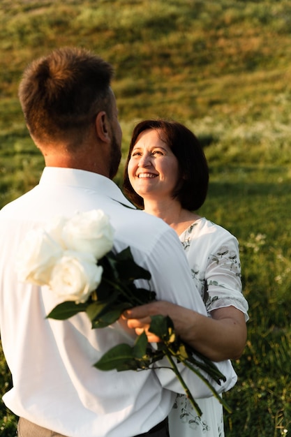 A middle-aged man hugs a woman of European appearance who is holding flowers from her husband in her hands. portrait of a couple in love at sunset