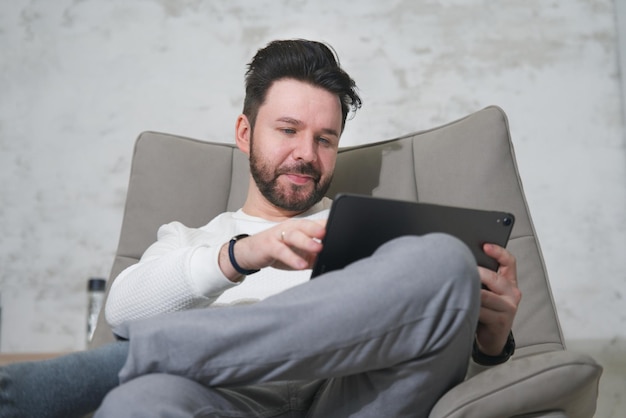 Мужчина средних лет использует свой планшетный ноутбук, сидит и читает электронную книгу или смотрит фильм