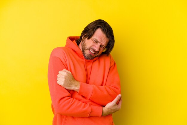 Middle aged man isolated on yellow wall massaging elbow, suffering after a bad movement