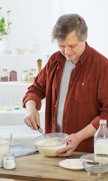 Uomo di mezza età che impasta la pasta del pancake sulla cucina bianca