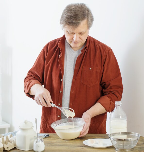 Middle-aged man kneading pancake dough on white kitchen